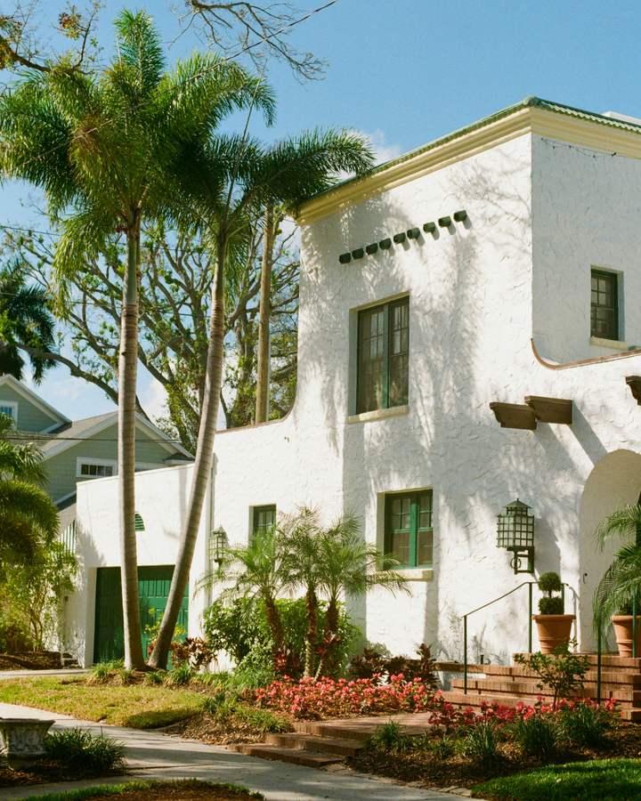 A white stucco home framed by palms and a planted border.